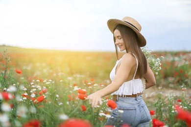 Photo of Smiling woman in hat touching wildflowers in meadow