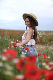 Photo of Smiling woman in hat touching wildflowers in meadow
