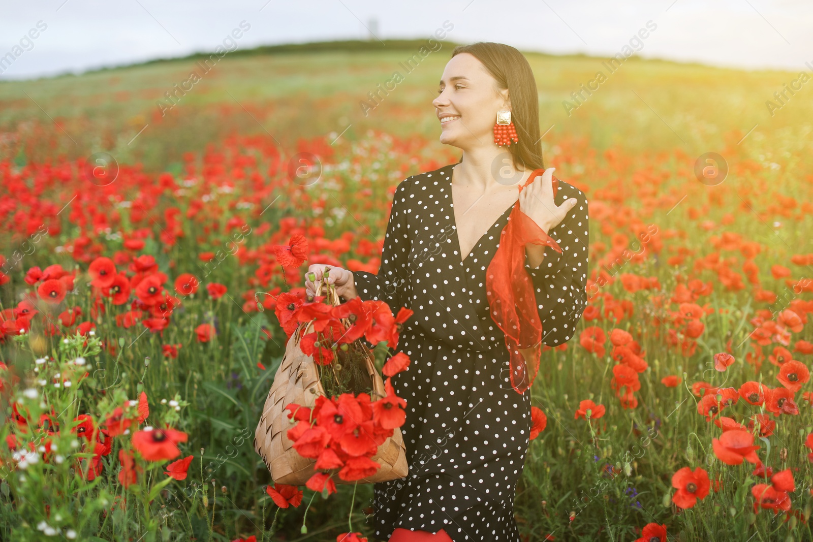 Smiling woman with bag and handkerchief among red poppy flowers in morning wildflower meadow Photo of Smiling woman with bag and handkerchief among red poppy flowers in morning wildflower meadow