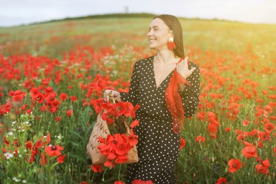 Photo of Smiling woman with bag and handkerchief among red poppy flowers in morning wildflower meadow