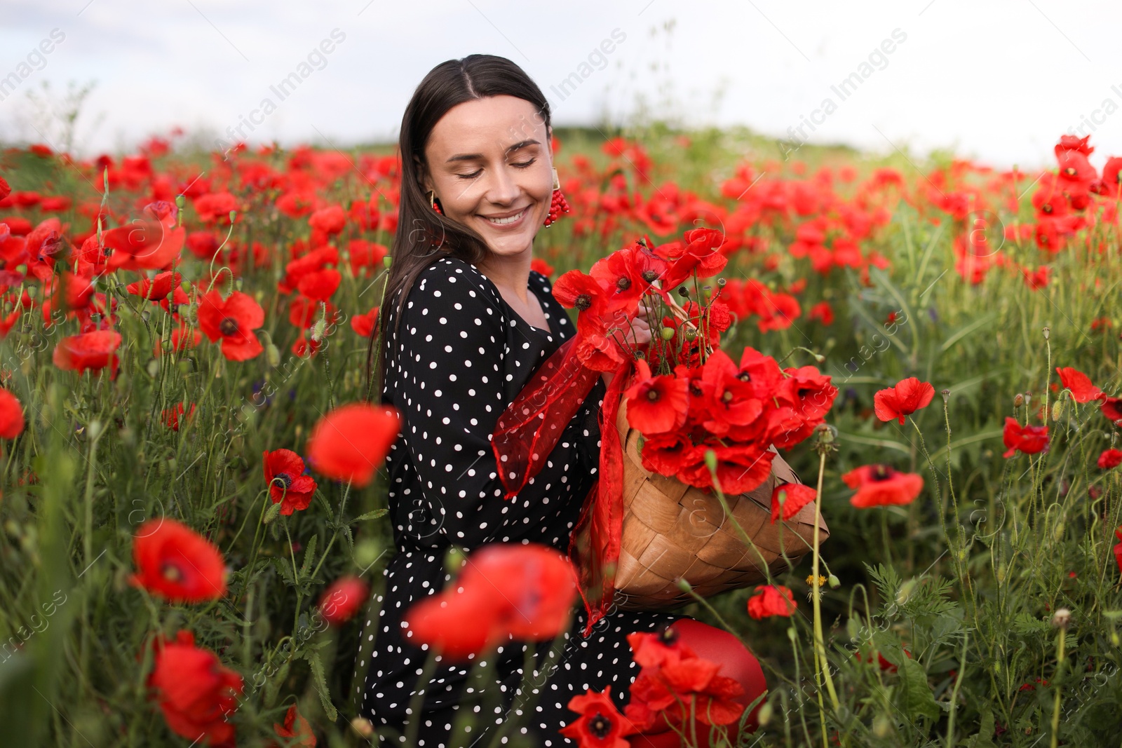 Photo of Smiling woman with bag among red poppy flowers in wildflower meadow