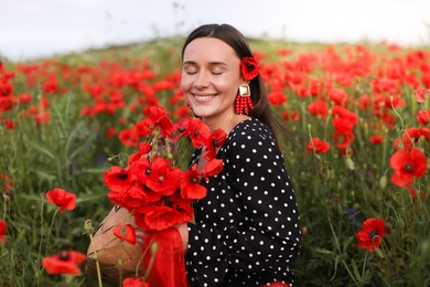 Photo of Smiling woman with bag among red poppy flowers in wildflower meadow