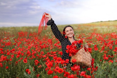 Photo of Smiling woman with bag and handkerchief among red poppy flowers in wildflower meadow