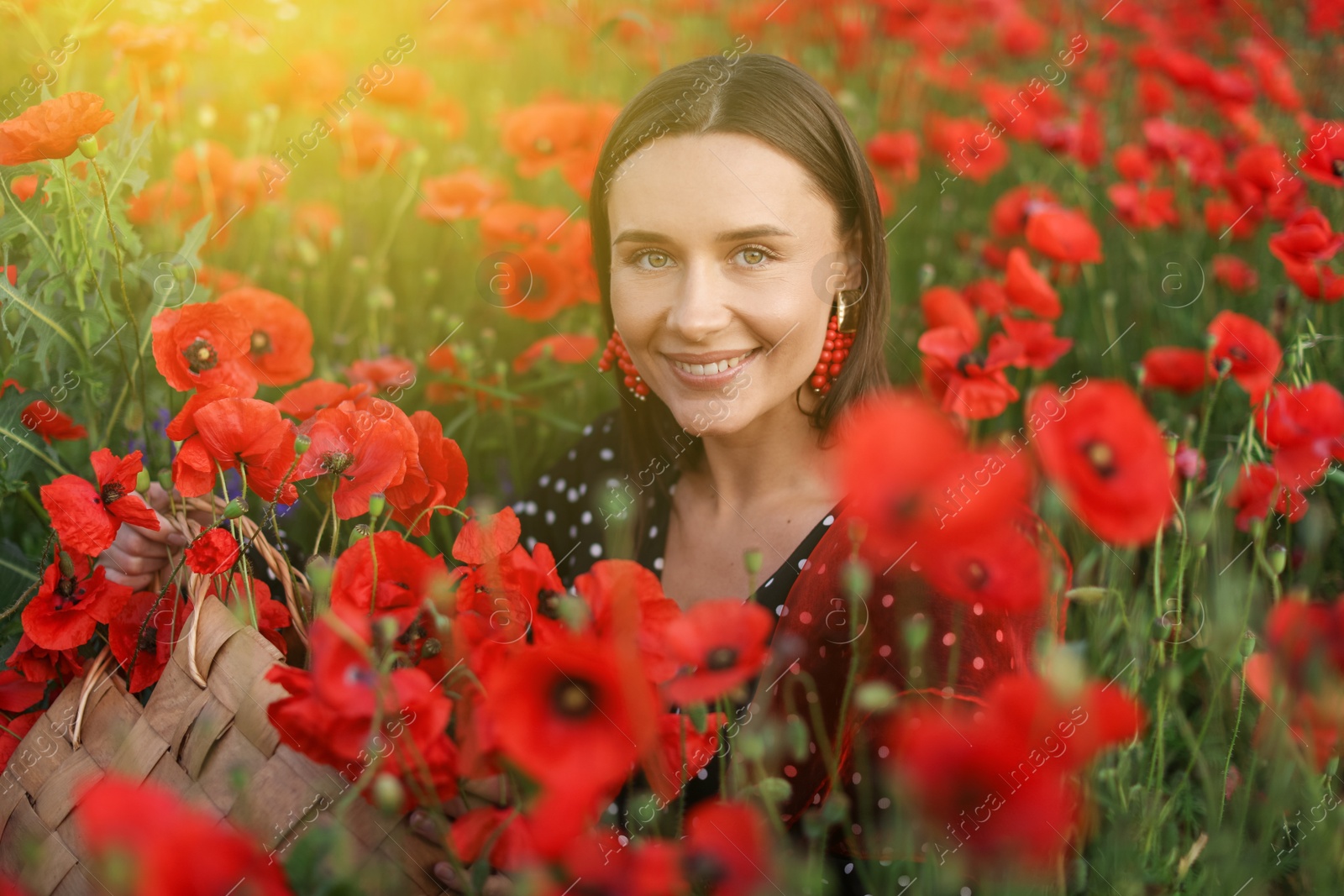 Photo of Portrait of smiling woman with bag among red poppy flowers in wildflower meadow