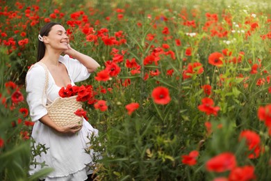Photo of Smiling woman with bag among red poppy flowers in wildflower meadow