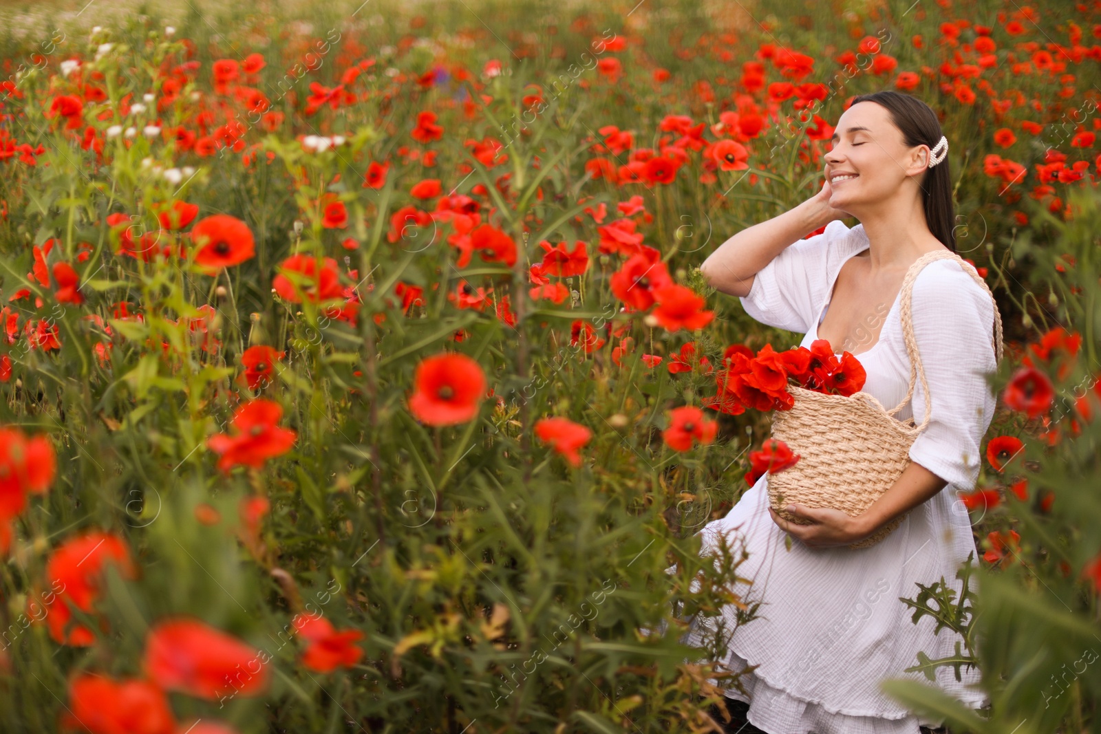 Smiling woman with bag among red poppy flowers in wildflower meadow Photo of Smiling woman with bag among red poppy flowers in wildflower meadow
