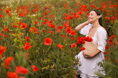 Photo of Smiling woman with bag among red poppy flowers in wildflower meadow