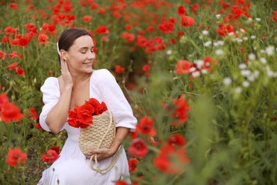 Photo of Smiling woman with bag among red poppy flowers in wildflower meadow