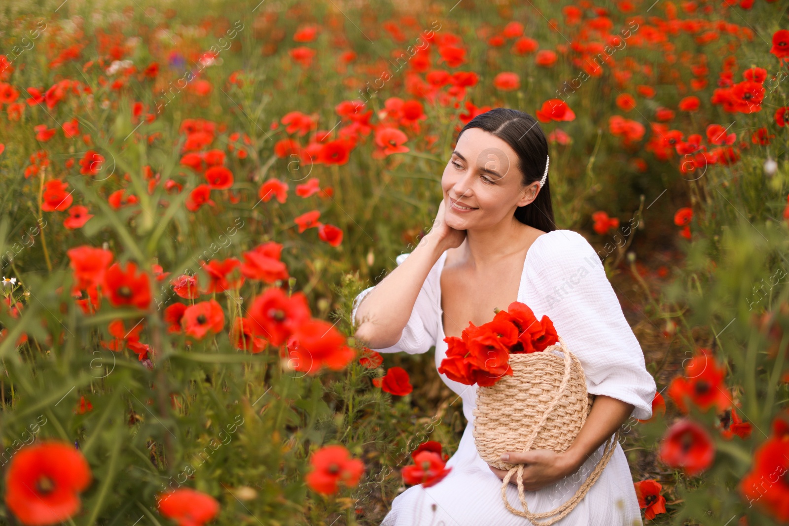 Smiling woman with bag among red poppy flowers in wildflower meadow Photo of Smiling woman with bag among red poppy flowers in wildflower meadow