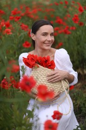 Photo of Smiling woman with bag among red poppy flowers in wildflower meadow
