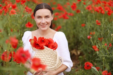 Photo of Portrait of smiling woman with bag among red poppy flowers in wildflower meadow