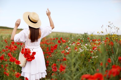 Photo of Woman in hat with bag of poppy flowers in wildflower meadow, back view