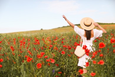 Photo of Woman in hat with bag of poppy flowers in wildflower meadow, back view