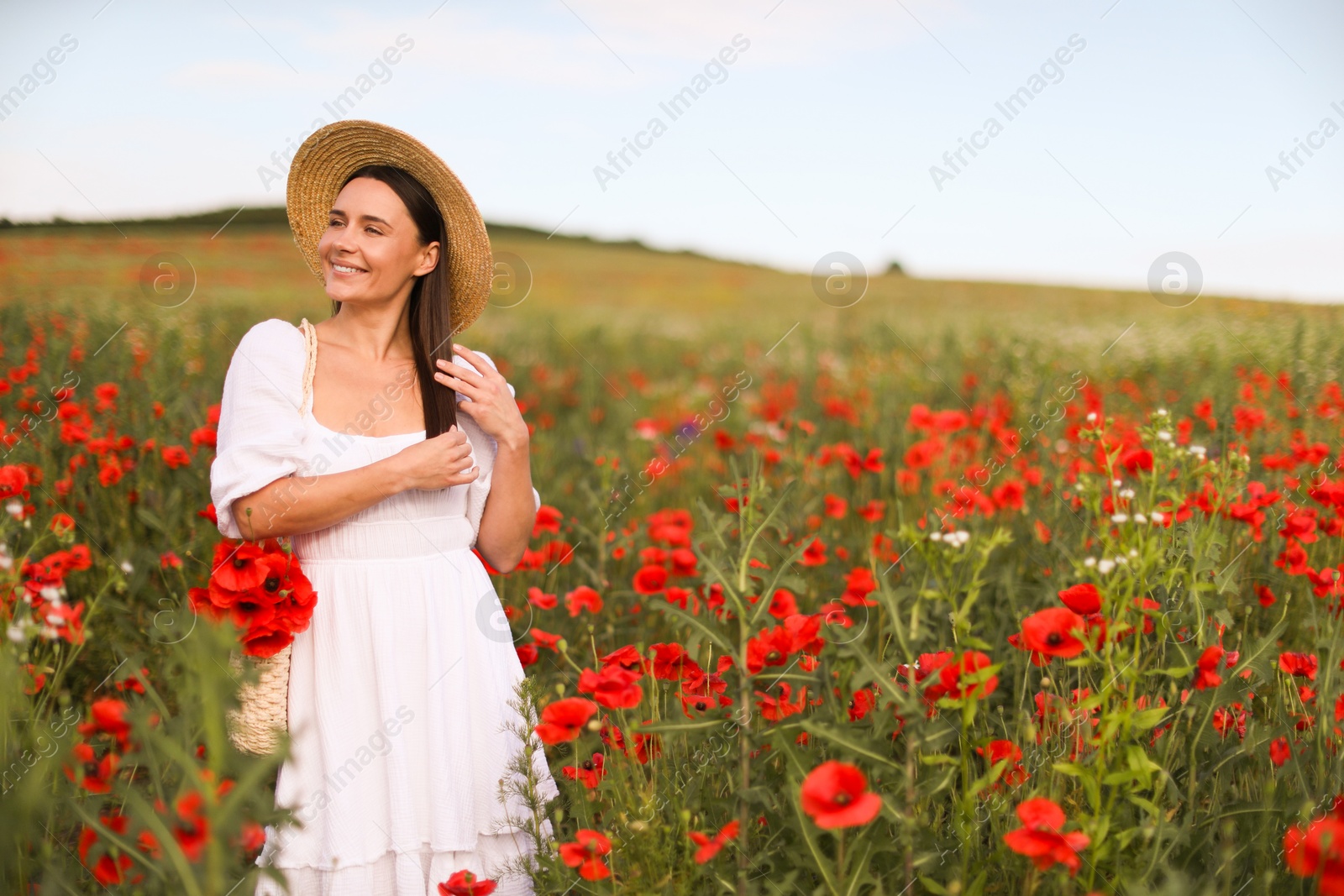 Photo of Smiling woman in hat with bag of poppy flowers in wildflower meadow