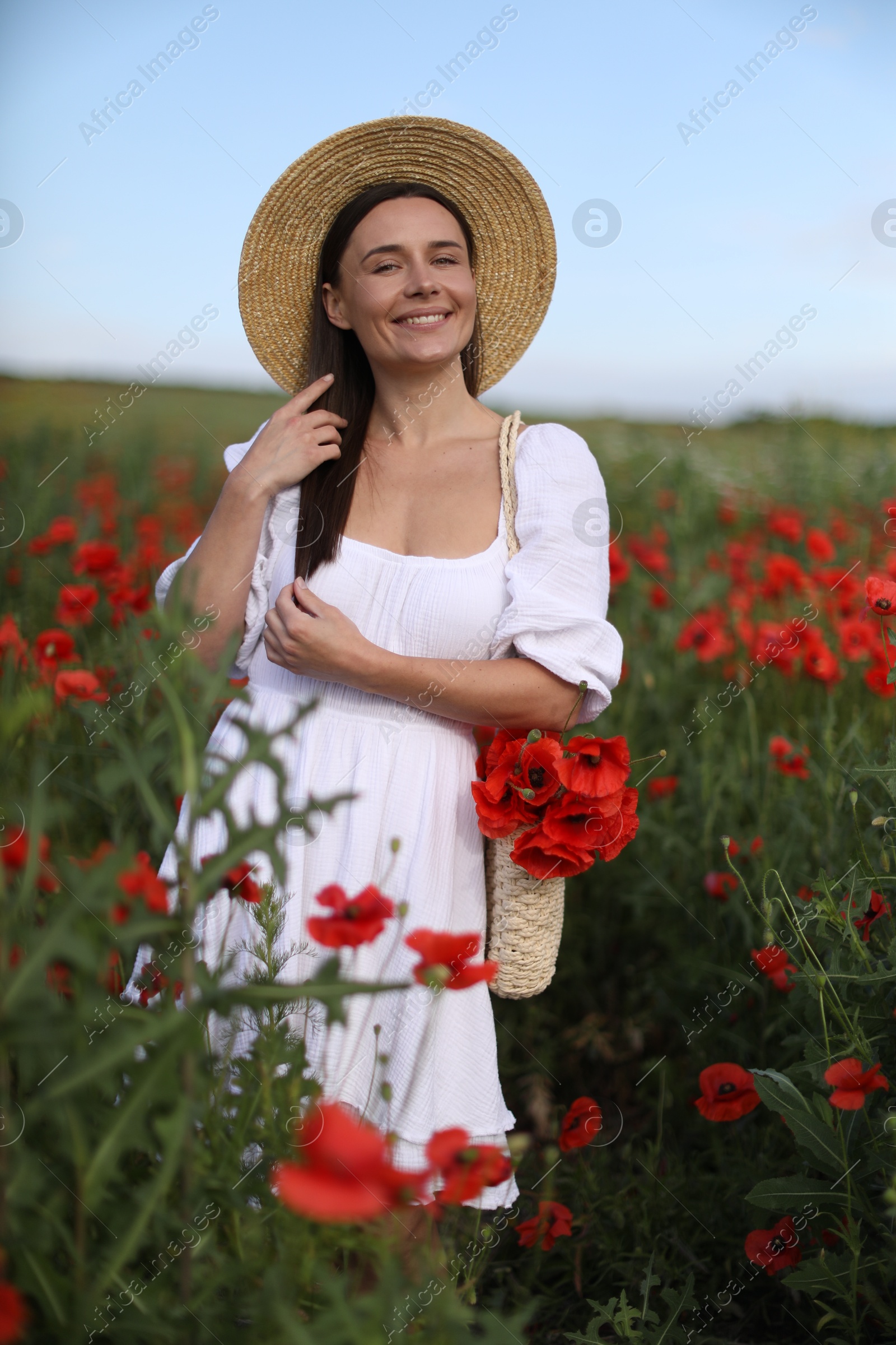 Photo of Portrait of smiling woman in hat with bag of poppy flowers in wildflower meadow
