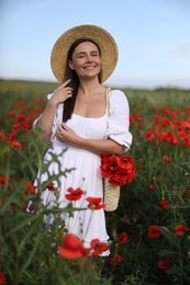 Photo of Portrait of smiling woman in hat with bag of poppy flowers in wildflower meadow