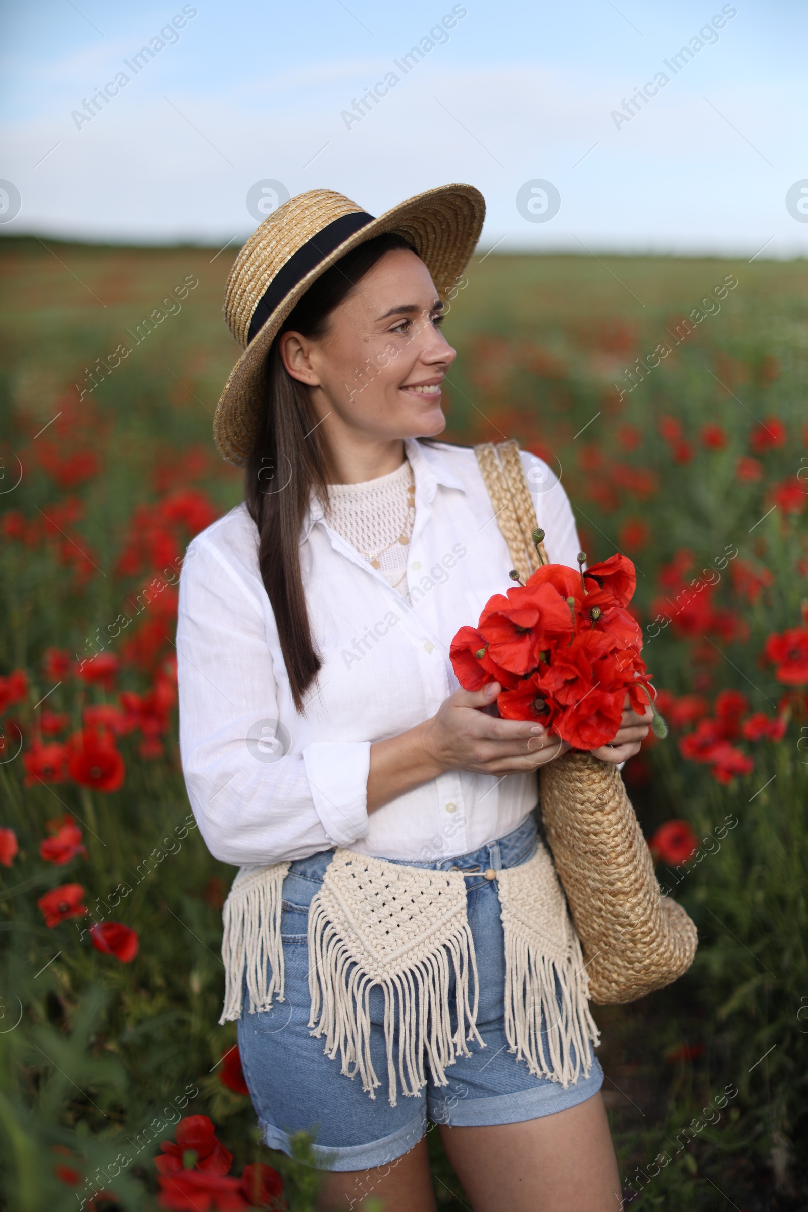 Photo of Smiling woman in hat with bag of poppy flowers in wildflower meadow
