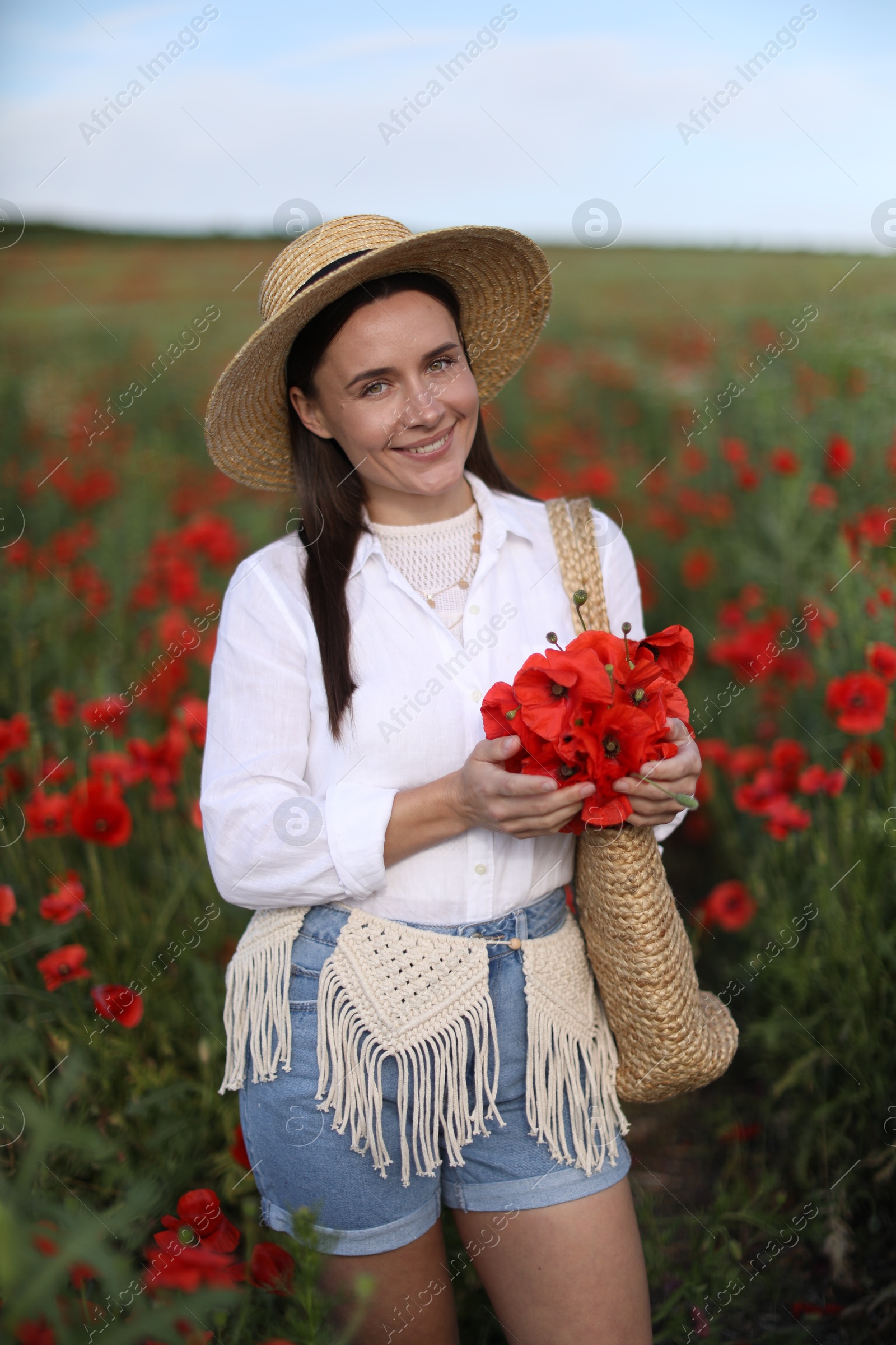 Photo of Portrait of smiling woman in hat with bag of poppy flowers in wildflower meadow