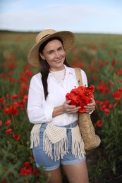 Photo of Portrait of smiling woman in hat with bag of poppy flowers in wildflower meadow