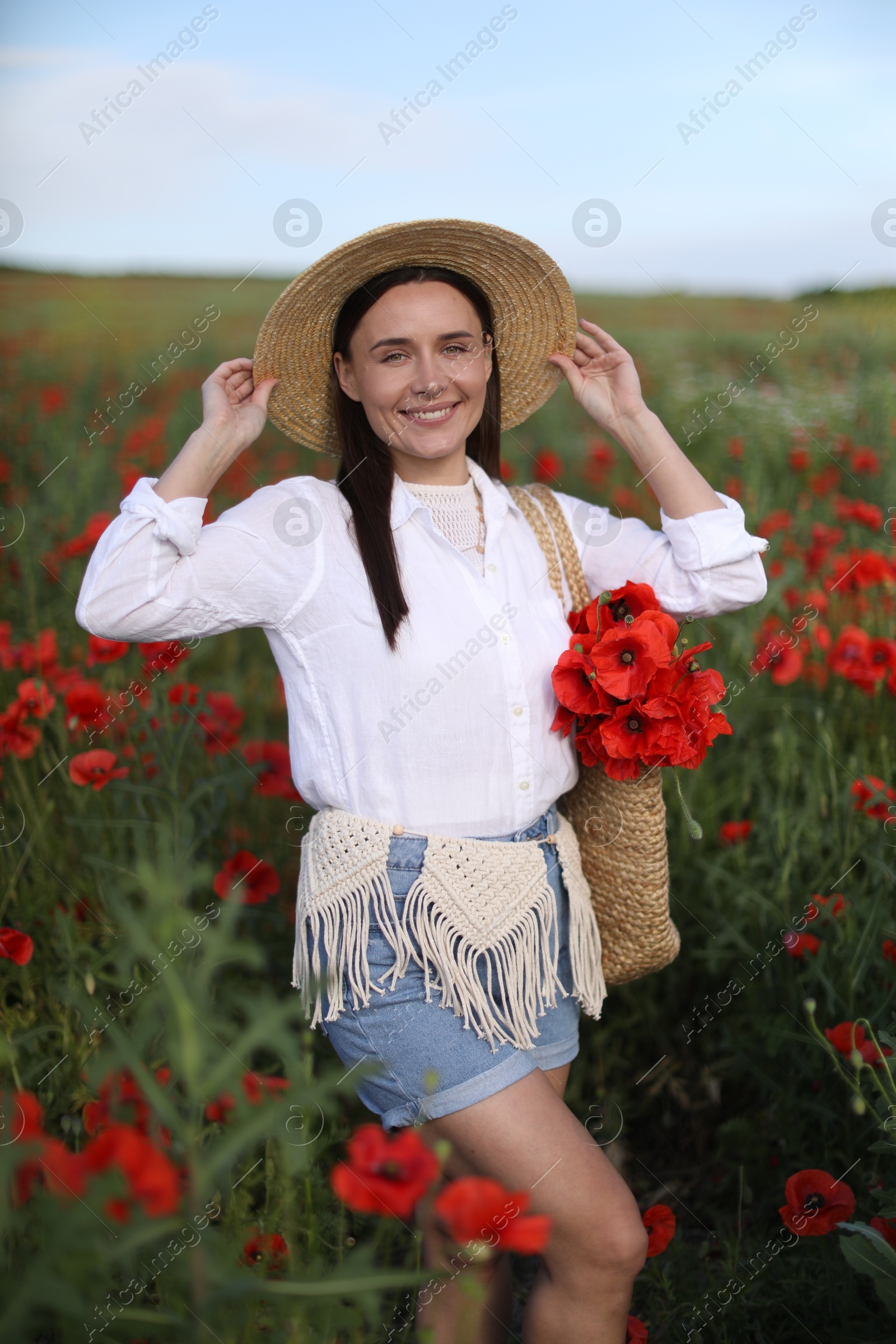Photo of Portrait of smiling woman in hat with bag of poppy flowers in wildflower meadow