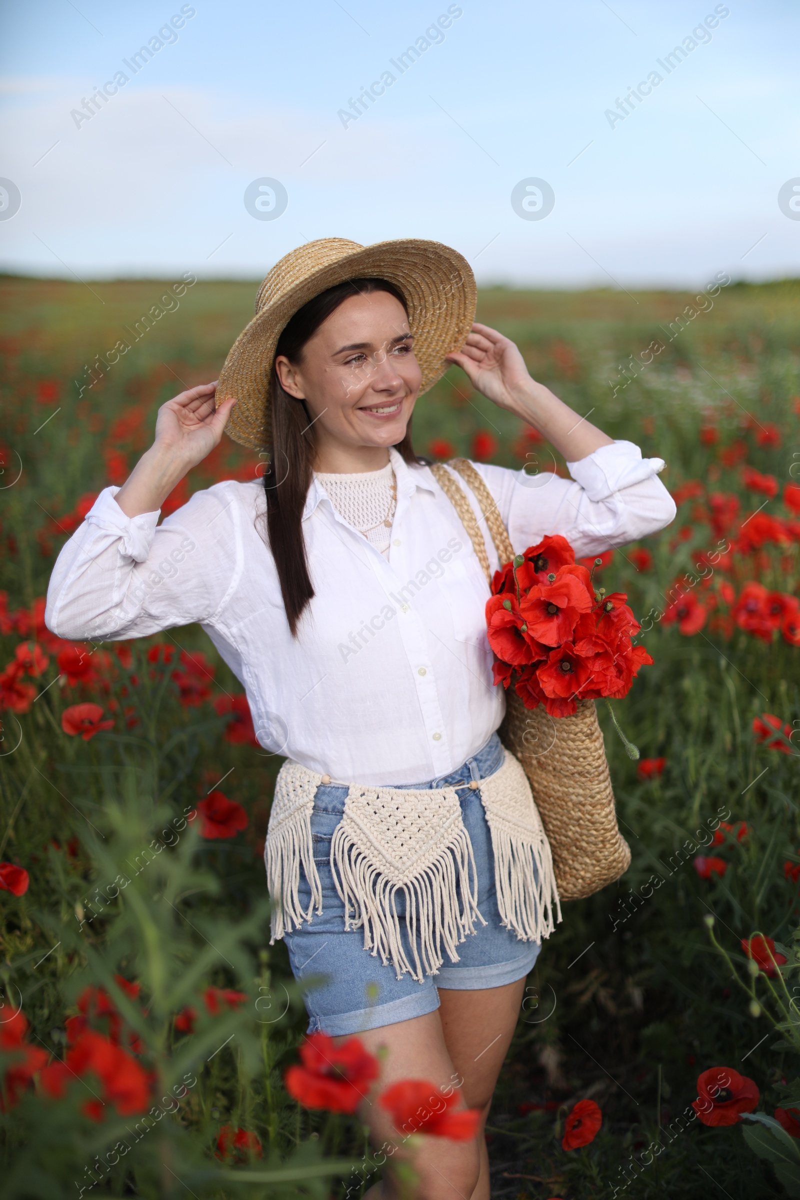 Smiling woman in hat with bag of poppy flowers in wildflower meadow Photo of Smiling woman in hat with bag of poppy flowers in wildflower meadow