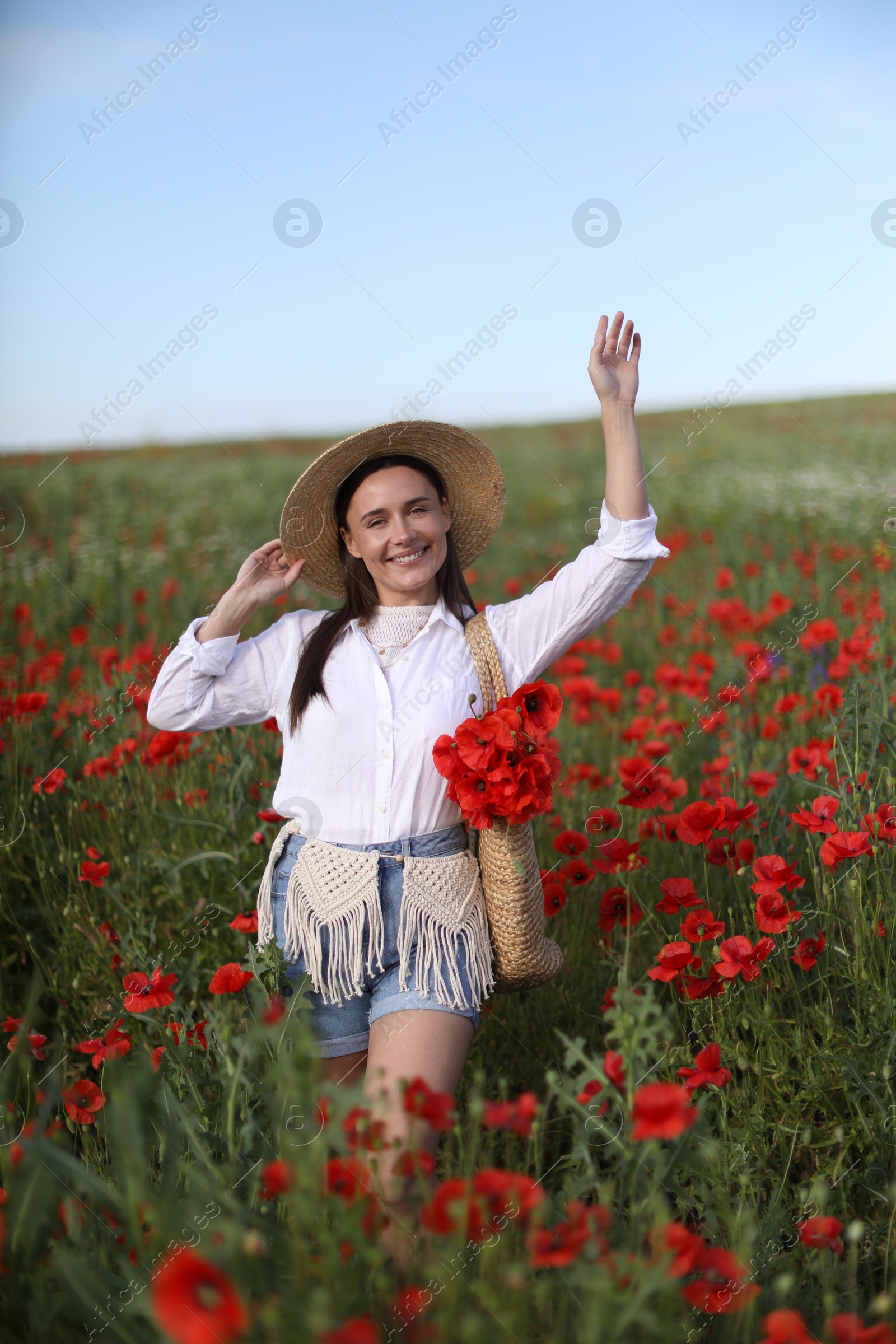 Photo of Smiling woman in hat with bag of poppy flowers walking across wildflower meadow