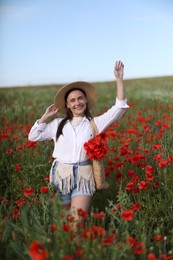 Photo of Smiling woman in hat with bag of poppy flowers walking across wildflower meadow