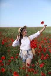 Photo of Smiling woman in hat with bag of poppy flowers walking across wildflower meadow