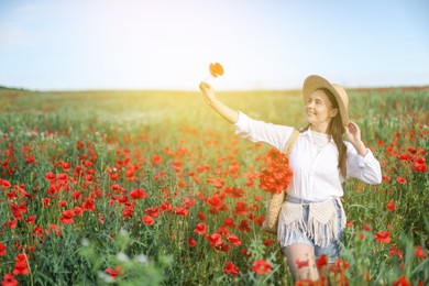 Photo of Smiling woman in hat with bag of poppy flowers walking across wildflower meadow in morning