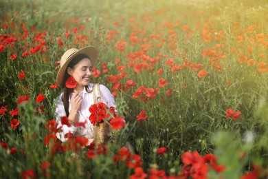 Photo of Smiling woman in hat with bag among red poppy flowers in morning wildflower meadow
