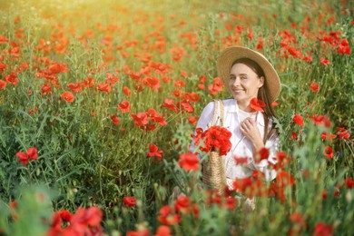 Photo of Smiling woman in hat with bag among red poppy flowers in morning wildflower meadow