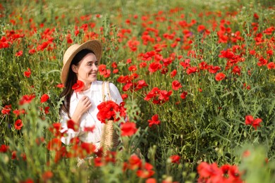 Photo of Smiling woman in hat with bag among red poppy flowers in morning wildflower meadow