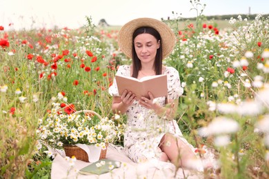 Photo of Smiling woman in hat reading book in wildflower meadow