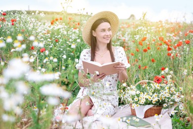 Photo of Smiling woman in hat with book in morning wildflower meadow