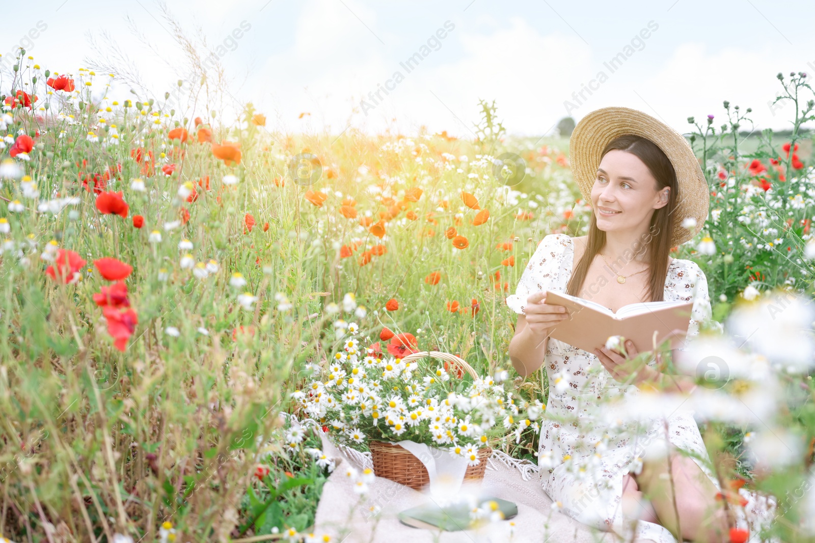 Smiling woman in hat with book in morning wildflower meadow Photo of Smiling woman in hat with book in morning wildflower meadow