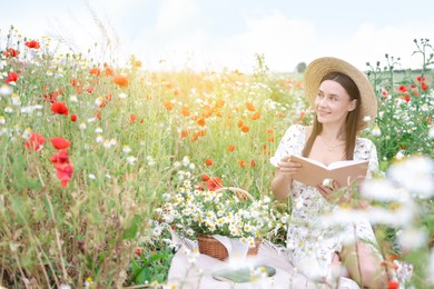 Photo of Smiling woman in hat with book in morning wildflower meadow