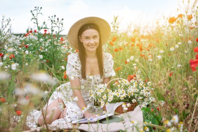 Photo of Smiling woman in hat with book in morning wildflower meadow