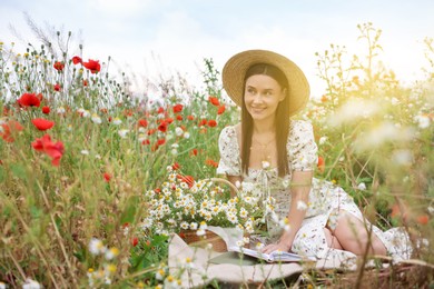 Photo of Smiling woman in hat with book in morning wildflower meadow