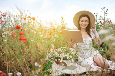 Photo of Smiling woman in hat reading book in morning wildflower meadow