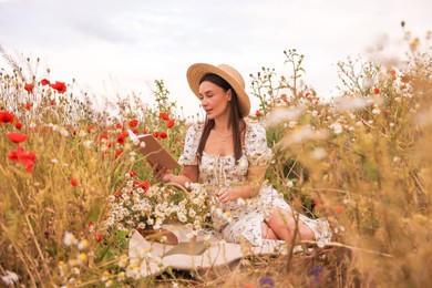 Photo of Beautiful woman in hat reading book in morning wildflower meadow
