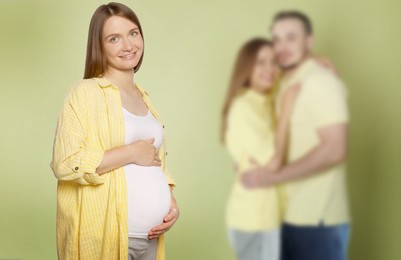 Image of Surrogate mother and intended parents against olive color background, selective focus