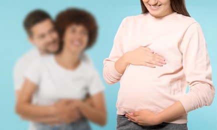 Image of Surrogate mother and intended parents against light blue background, selective focus