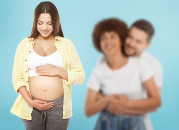 Image of Surrogate mother and intended parents against light blue background, selective focus