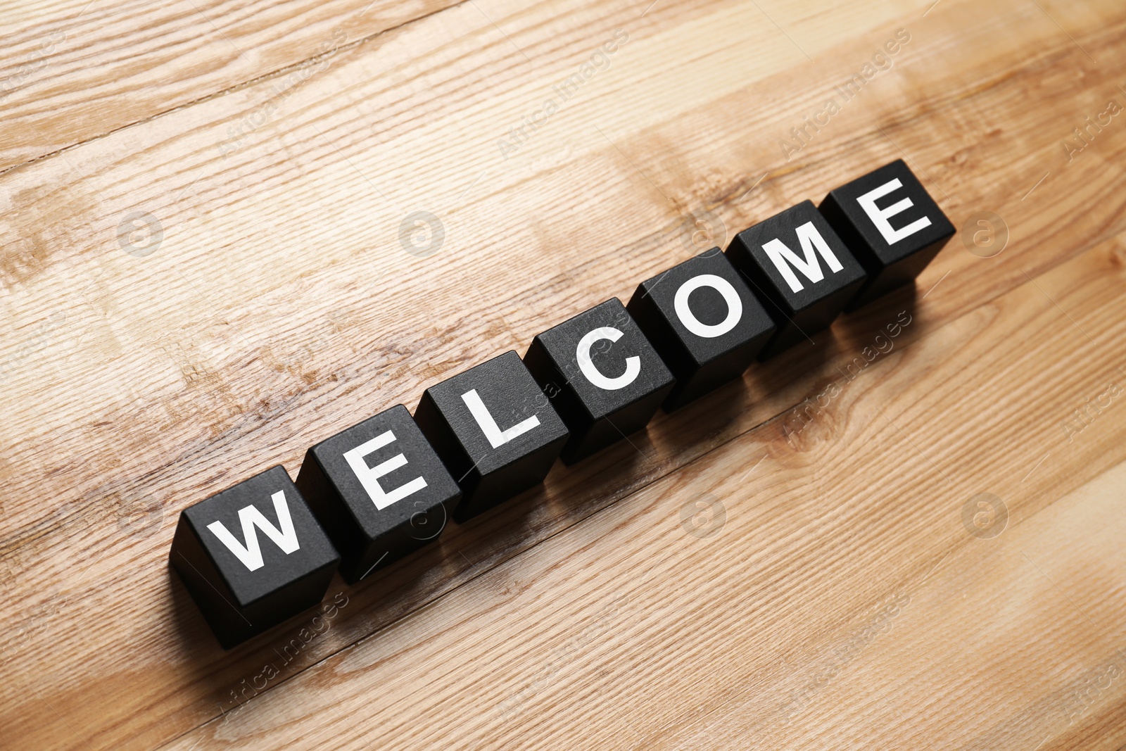 Word Welcome made of black cubes on wooden table, above view Image of Word Welcome made of black cubes on wooden table, above view
