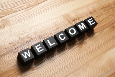 Image of Word Welcome made of black cubes on wooden table, above view