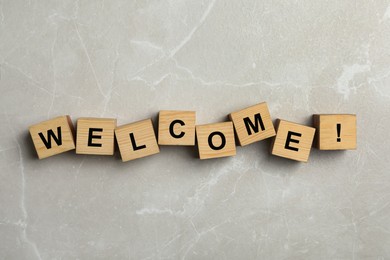 Image of Word Welcome and exclamation mark made of wooden cubes on grey marble background, top view