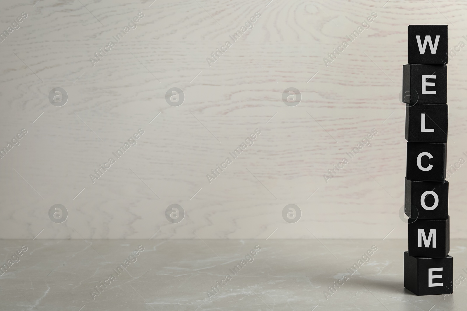 Word Welcome made of stacked black cubes on grey marble table, space for text Image of Word Welcome made of stacked black cubes on grey marble table, space for text