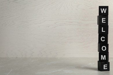 Image of Word Welcome made of stacked black cubes on grey marble table, space for text