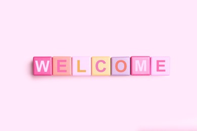 Image of Word Welcome made of colorful cubes on pink background, top view