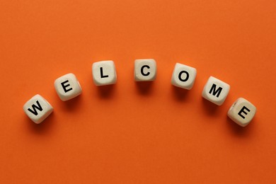 Image of Word Welcome made of wooden cubes on orange background, top view